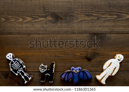 Fresh halloween gingerbread. Icing cookies in shape of halloween evils like black cat, skeleton, bat on dark wooden background top view copy space