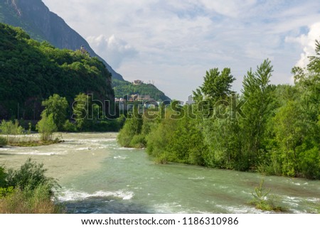 Isarco river in spring time with  a castle and a church high upp in mountain in background, picture from Italy.