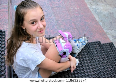 Long hair beautiful smiling girl in roller skates sitting on stairs and looking 