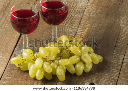 An image of two drinking glasses with red wine  and a bunch of grape, on an old wooden table. 