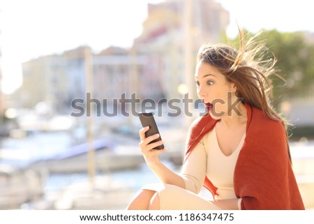 Amazed woman watching on line content in a smart phone in the street