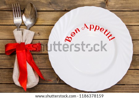 Empty dish and cutlery on wooden background close up view from top. Dinner set with text or lettering. Bon appetit
