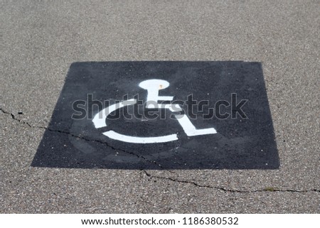 The handicap symbol painted white on the cement concrete of the parking space.