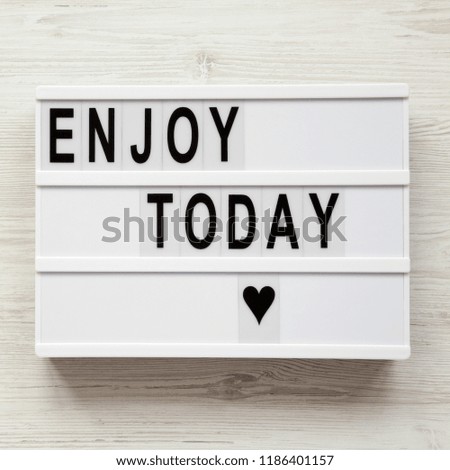 'Enjoy today' word on lightbox over white wooden background, from above. Top view, overhead, flat lay. Copy space.