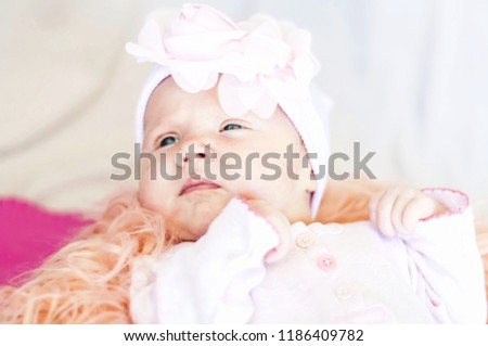 A cute Caucasian newborn baby girl with a flower head band lying on a bed. Curious look. New life concept. One month old baby.