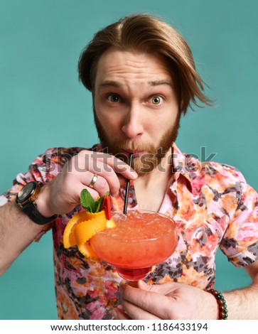 Young man in hat and sunglasses drinking margarita cocktail drink juice happy looking at camera laughing over light green background