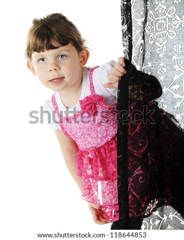 An adorable preschooler dressed in neon pink peeking around a black curtain.  On a white background.