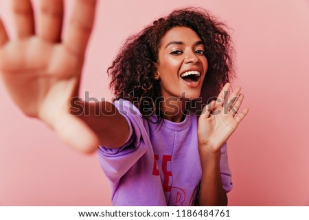 Joyful dark-eyed girl smiling while making selfie. Amazing brunette african lady fooling around in studio.