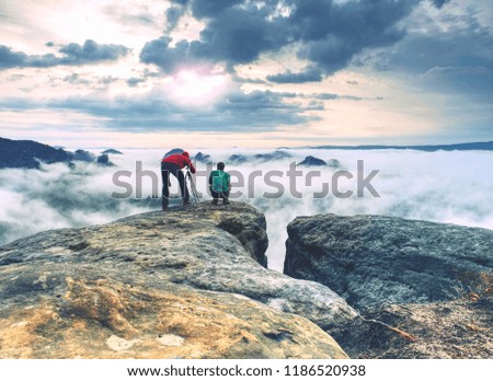 Photographer down on knees takes photos with mirror camera on exposed rock. Tourist using tripod to take pictures of misty fall landscape