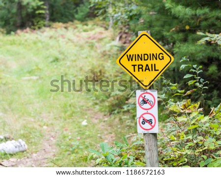 Winding trail sign along the edge of a path through the woods. Symbols icons for no motorbikes, motorcycles, atv or four-wheelers. Concepts of recreation, nature and outdoors