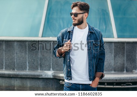 A stylish man with a beard cleans his glasses with a T-shirt. Street photo