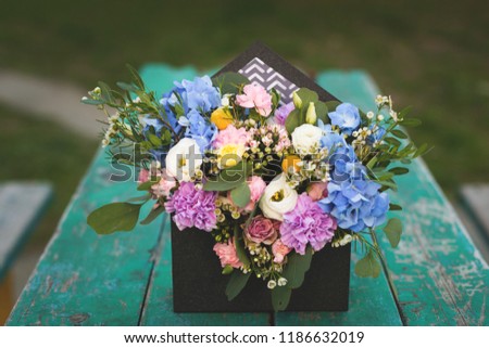 Image of flowers arrangement with hydrangea, eustoma, spray yellow and violet roses, pink carnations, eucaliptus, waxflowers. Mixed flowers bouquet in black envelope box on the turquoise wooden table