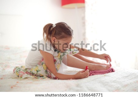 funny kid girl paints nails in the bedroom, the concept of make-up and beauty, happy childhood