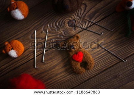 toy bear cub with heart made of wool and tools for dry felting, dark brown wooden background,