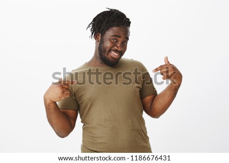 Confident guy assured in his charm and beauty. Portrait of energetic happy plump man in military t-shirt, smiling cheerfully and pointing at himself while bregging about own achievement over gray wall