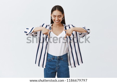 Girl bragging about new stylish shoes she bought. Portrait of charming happy dark-haired female in striped blouse, looking and pointing down with index fingers, learning how skate on rollerblades