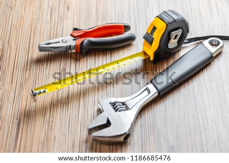 Adjustable pliers, Wrench and measuring tape on wooden table background. Working tools