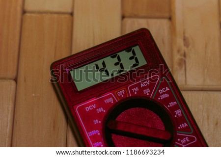 Red digital measuring multimeter on wooden floor. It shows 4.33V or fully charged battery. Includes voltmeter, ampermeter, ohmmeter.