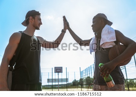 Side view portrait of two basketball players doing high-five against blue sky after match in outdoor court, copy space