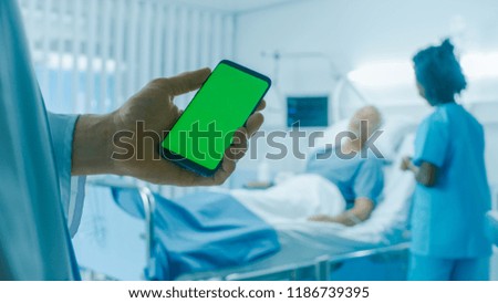 In the Hospital Doctor Holds Green Screen Mobile Phone, In the Background Patients Lies in Bed while Nurse Checks Him.