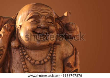 Hotei or the laughing Buddha is a wooden statue on a brown background..