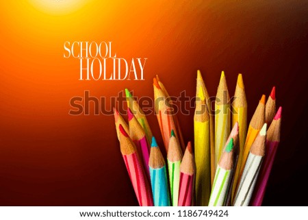 Concept of School holiday  with inscription, color pencils on black background with flare. 
