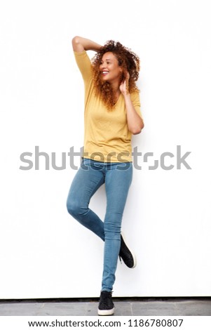Full body portrait of happy young woman with hands in curly hair against white wall