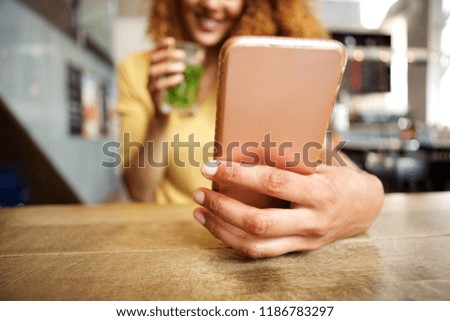Close up front portrait of happy young woman sitting at cafe with a drink, looking at mobile phone