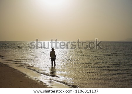 Dark silhouette of happy carefree lonely woman enjoying beautiful sunrise standing in sunny calm golden sea water at empty summer tropical beach. Happy beach holiday, vacation and travel concepts.