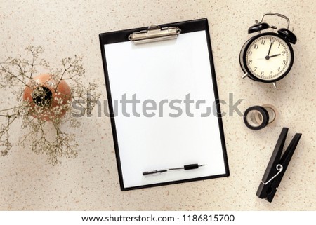 Terrazzo desk with a black office mockup pad, a vase with dried white flowers, an alarm clock and a large clip