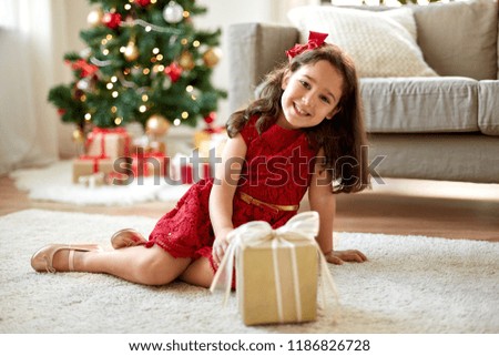 christmas, holidays and childhood concept - happy girl with gift box at home