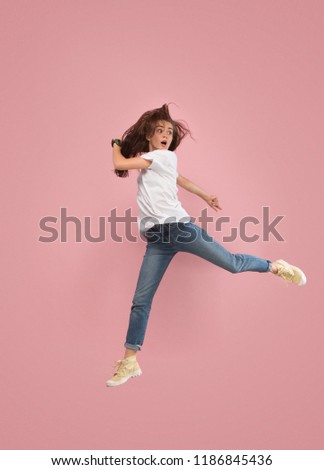 Freedom in moving. Mid-air shot of pretty frightened running away young woman jumping against pink studio background. Runnin girl in motion or movement. Human emotions and facial expressions concept