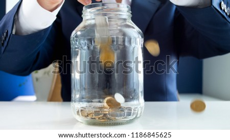 Closeup image of coins falling for businessmans hands in glass jar. Concept of wealth and richness