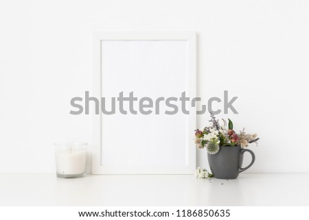White a4 portrait frame mockup with dried field wild flowers in vase and white candle on white wall background. Empty frame, poster mock up for presentation design. Template frame for text, lettering
