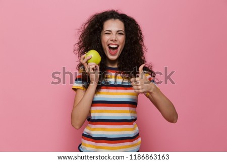 Photo of brunette woman 20s with curly hair smiling and holding green apple isolated over pink background