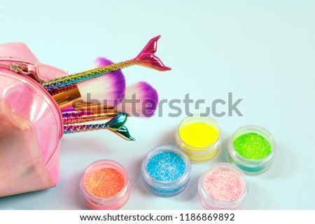 set of mermaid tail make-up brushes and colorful glitter eye shadows. Make up tools on pastel blue background.