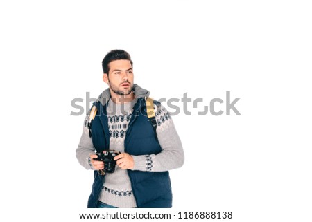 handsome young man with backpack holding camera and looking away isolated on white