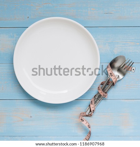 Top view Pink Measuring tape wrapped around fork and spoon with white dish on blue pastel color wooden table. dieting, weight loss and clean food concept