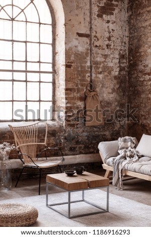 Table between pouf and couch in living room interior with window above armchair. Real photo