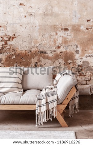 Patterned blanket and pillows on wooden grey couch against red brick wall in flat interior. Real photo