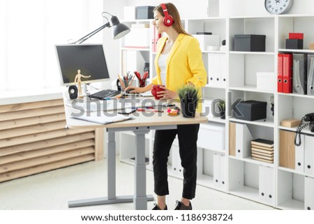 A young girl in headphones is working at the computer and is drinking from a red cup. Before the girl on the table is a magnetic board