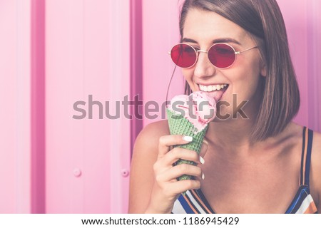 Portrait of young urban woman with ice cream on pastel pink background.