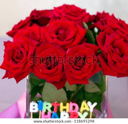 Candles of the letters "Happy birthday" in the background of a bouquet of red roses