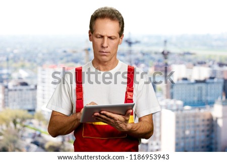 Middle aged engineer using digital tablet. Caucasian construction worker in uniform working on pc tablet. People, occupation, technology.