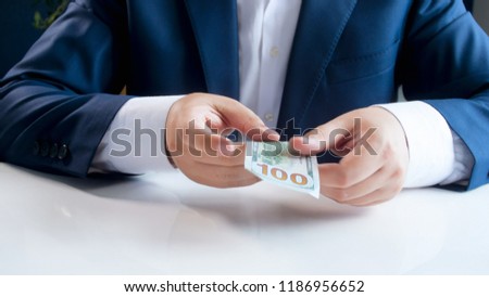 Closeup photo of businessman sitting behind desk and holding 100 US dollars bill