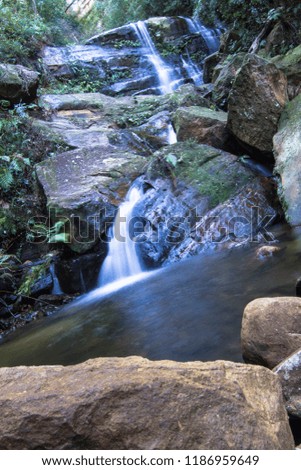 long exposure of mountain stream waterfall running between rocks with forest in background