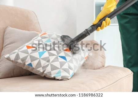 Janitor removing dirt from sofa cushion with steam cleaner, closeup Royalty-Free Stock Photo #1186986322