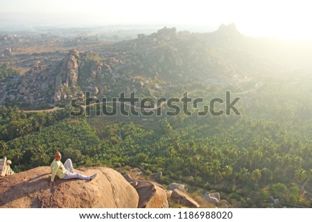 A handsome bald man in glasses sits on a sunset or dawn background in Hampi, on the top of the mountain. A brave man is extreme. India, Vijayanagar, karnataka, unesco.