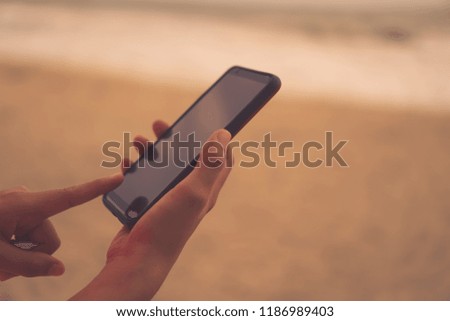 Woman hand using smartphone beautiful nature tropical beach ocean background. Business, financial, trade stock maket and social network concept.
