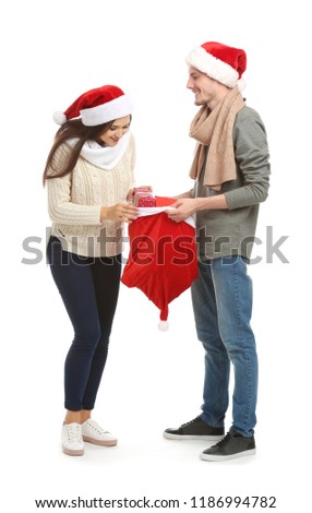 Young woman choosing gift from Christmas bag held by her husband on white background